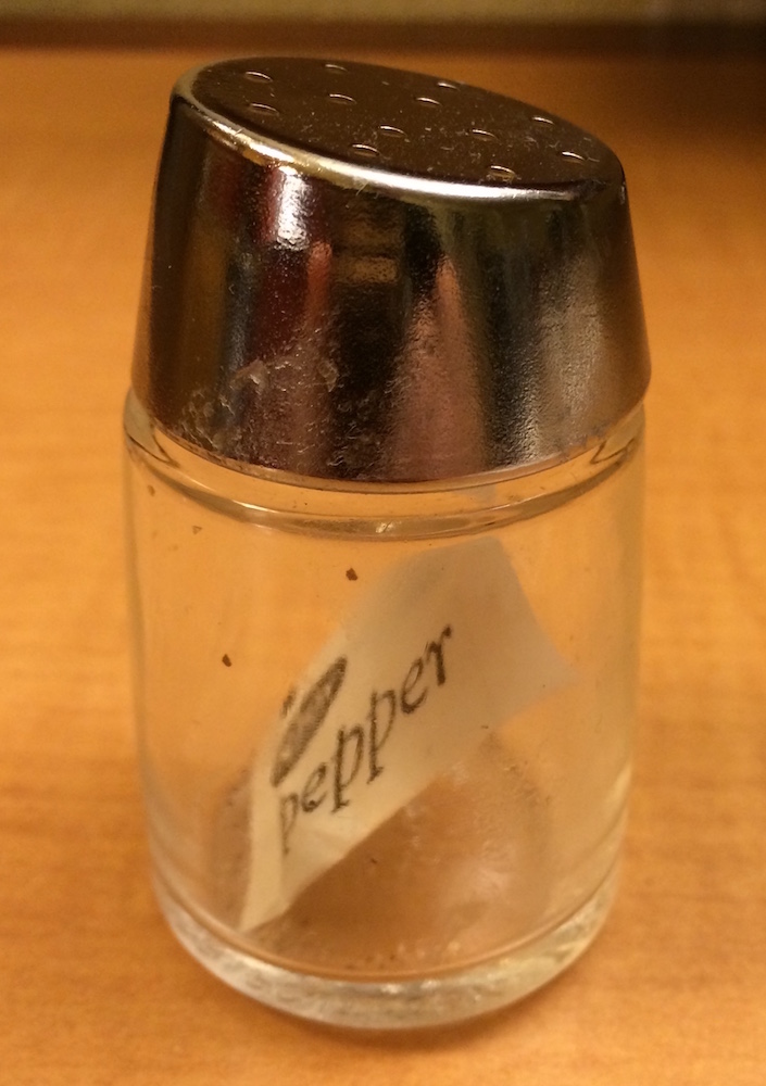 A photo of the glass pepper shaker containing just one packet of pepper.